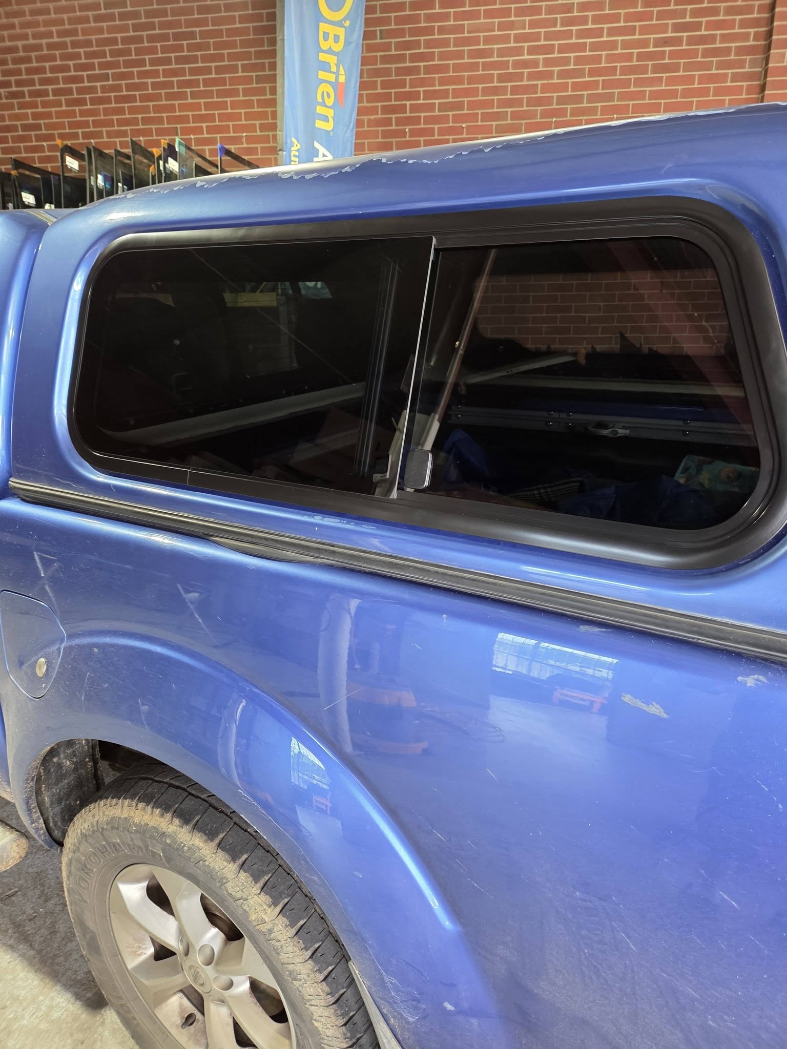 A blue Nissan Navara with a canopy, its sliding side window newly fitted, photographed inside the workshop